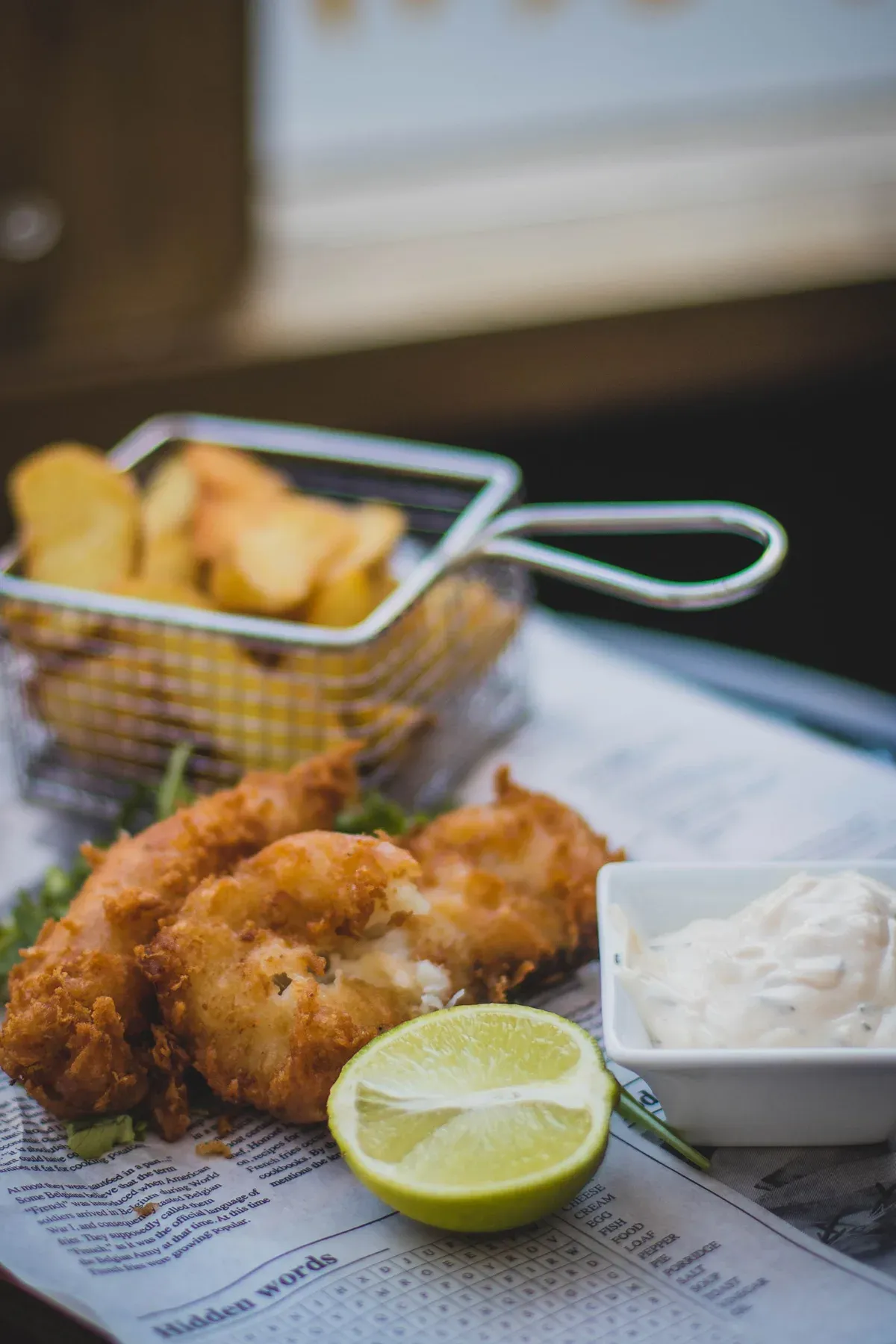 Battered fish and chips served on newspaper with tartare sauce